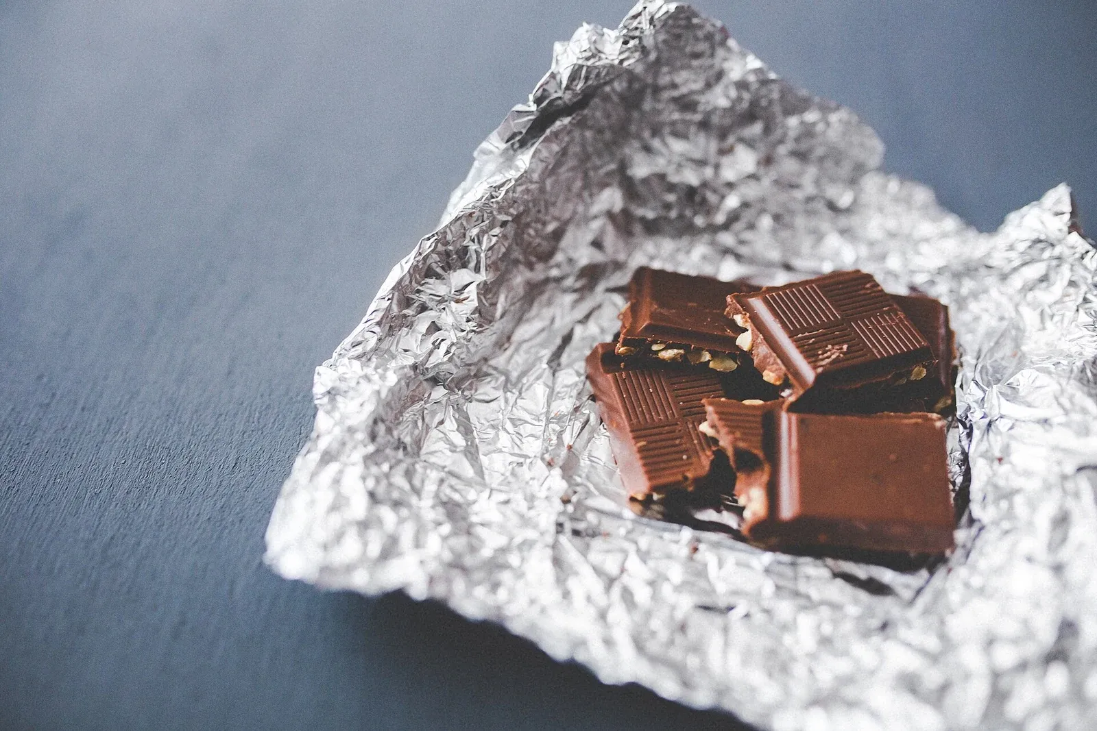 Carrés de chocolat entamés dans leur papier aluminium, posés sur une table sombre